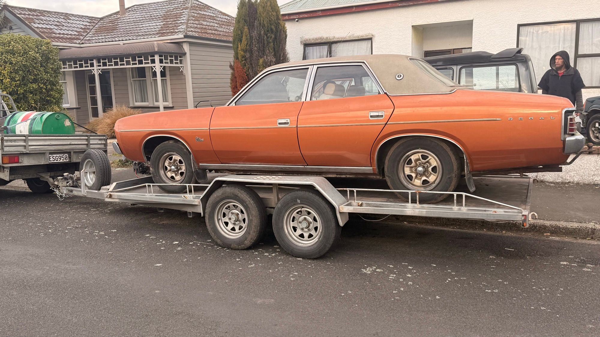 A copper Regal sedan strapped on Load and Tow's tandem-axle alloy car transporter, hitched behind the ute on a wet street.